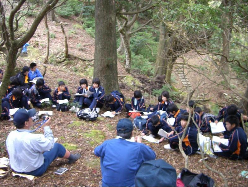 森林の中で中学生に森林の土壌を説明