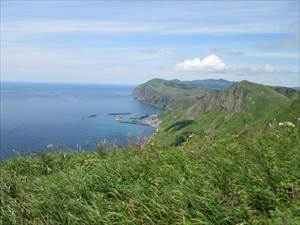 風が吹き抜ける草原の先に、集落と海岸線が見えます。