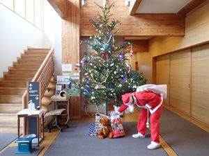 サンタに変装した職員がクリスマスツリーの下にぬいぐるみとお菓子入りの靴下を置く様子
