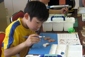 木粘土に野鳥図鑑を見ながら鳥の色付けをする子どもたち