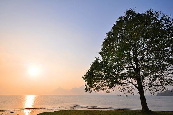 湖畔に昇る朝陽と朝靄に霞む中島