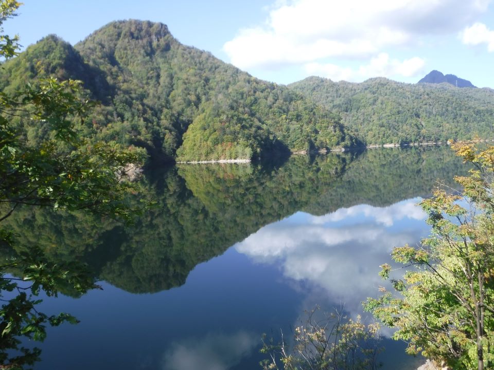 ダムの鏡面に映える森林と空