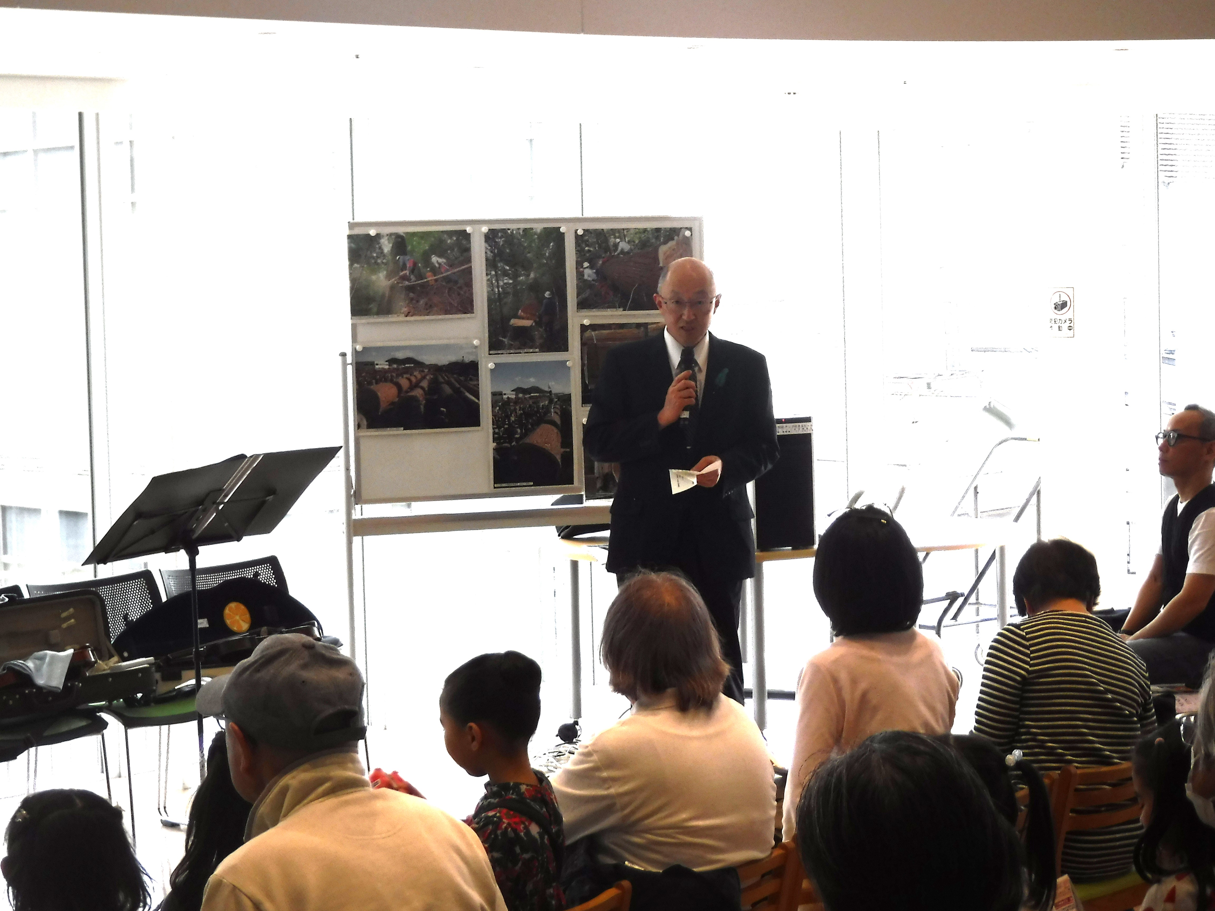 オーテピア２階の子ども読書コーナーで開かれた「森の音楽会」の様子。演奏の前に四国森林管理局の局長が挨拶を述べている。手前には観客の後ろ姿が映っている。