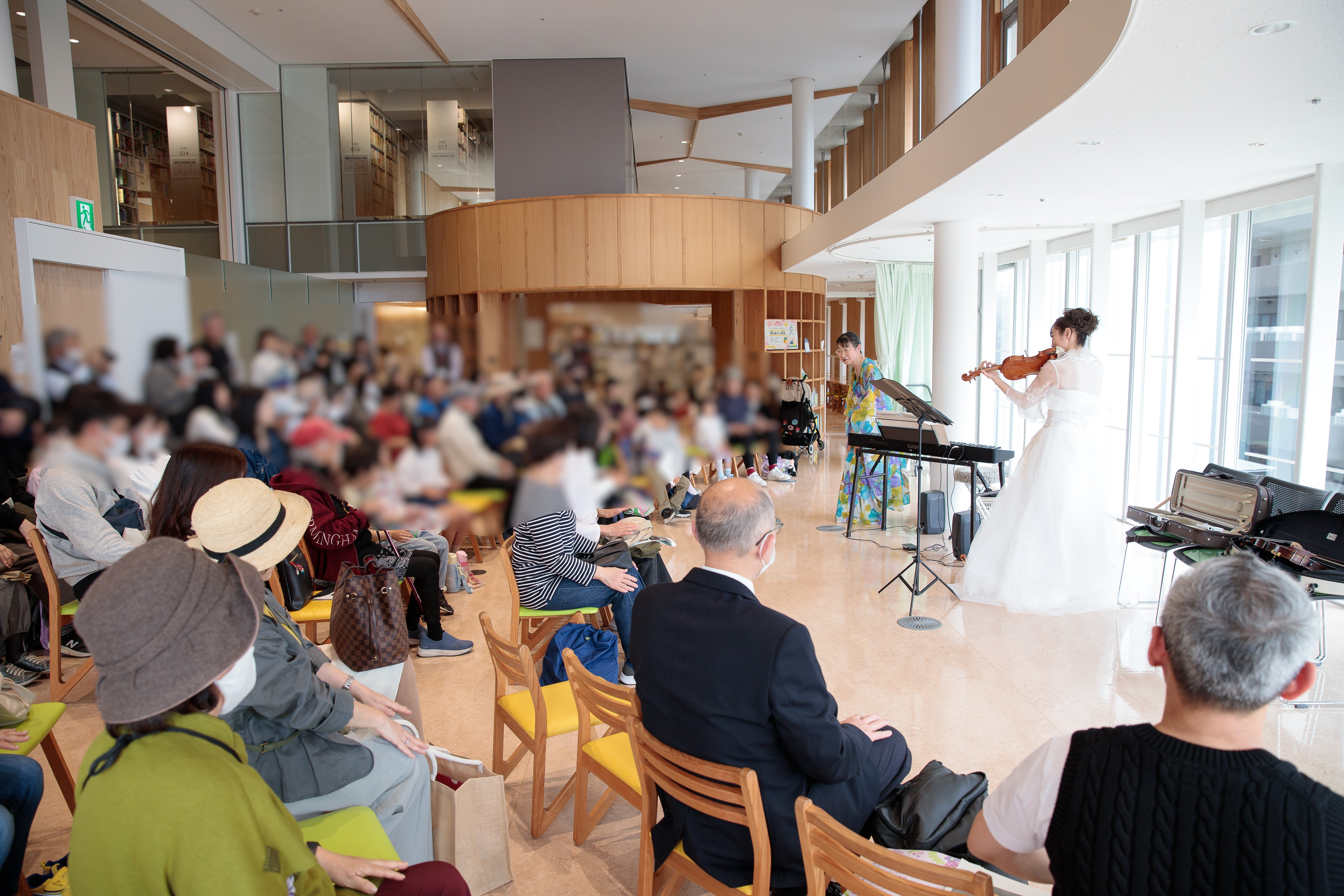 「森の音楽会」会場全体の様子。右側にはヴァイオリンとピアノの演奏者がきれいなドレスを着て演奏している姿。左側には観客が沢山写っている。立ち見の人もいる。